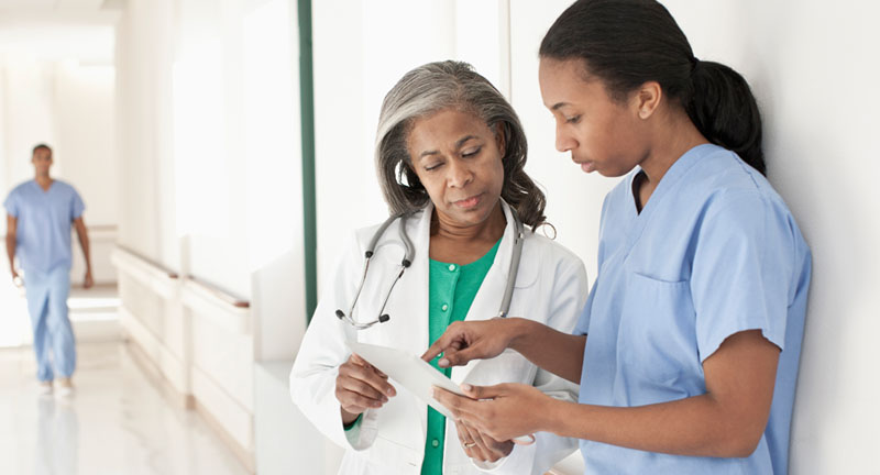 A female doctor and nurse in a hallway discussing a document